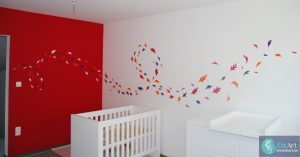 Wandschildering in babykamer van kleurrijke, dansende blaadjes.