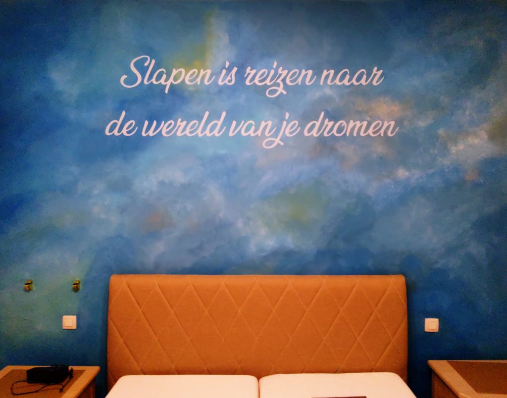 abstracte dromerige muurschildering in de slaapkamer met blauwe tinten en een toepasselijke spreuk boven het bed