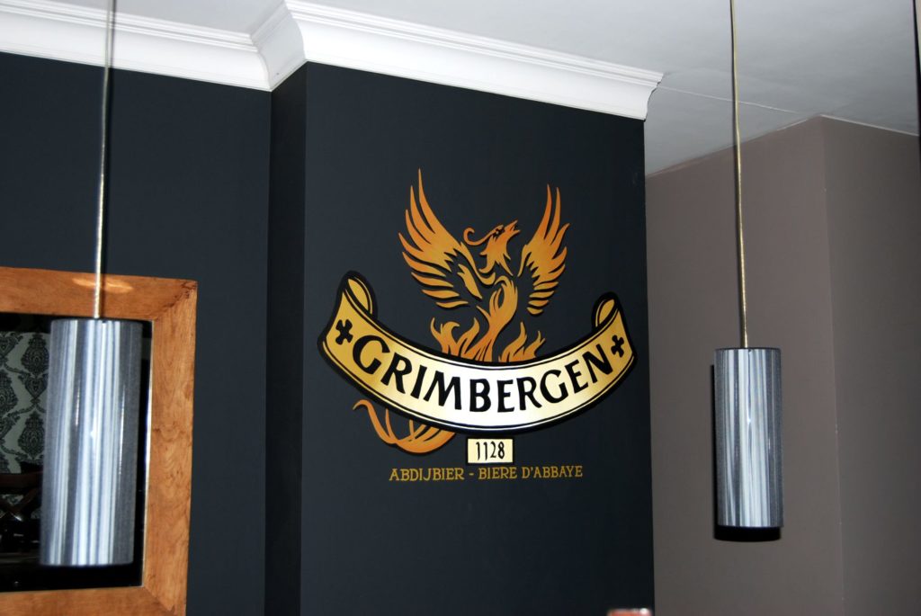 geschilderd logo van Grimbergen bier op een zwarte muur in een restaurant