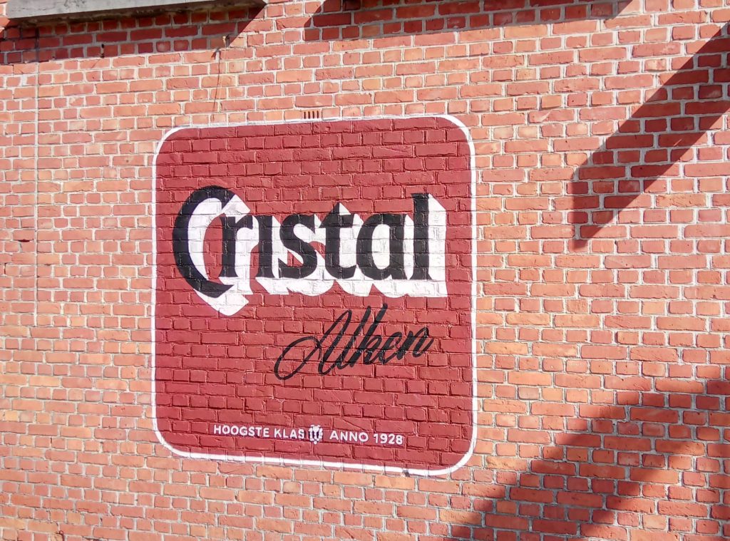 muurschildering van een oud bierkaartje van Cristal bier op een gevel van een café